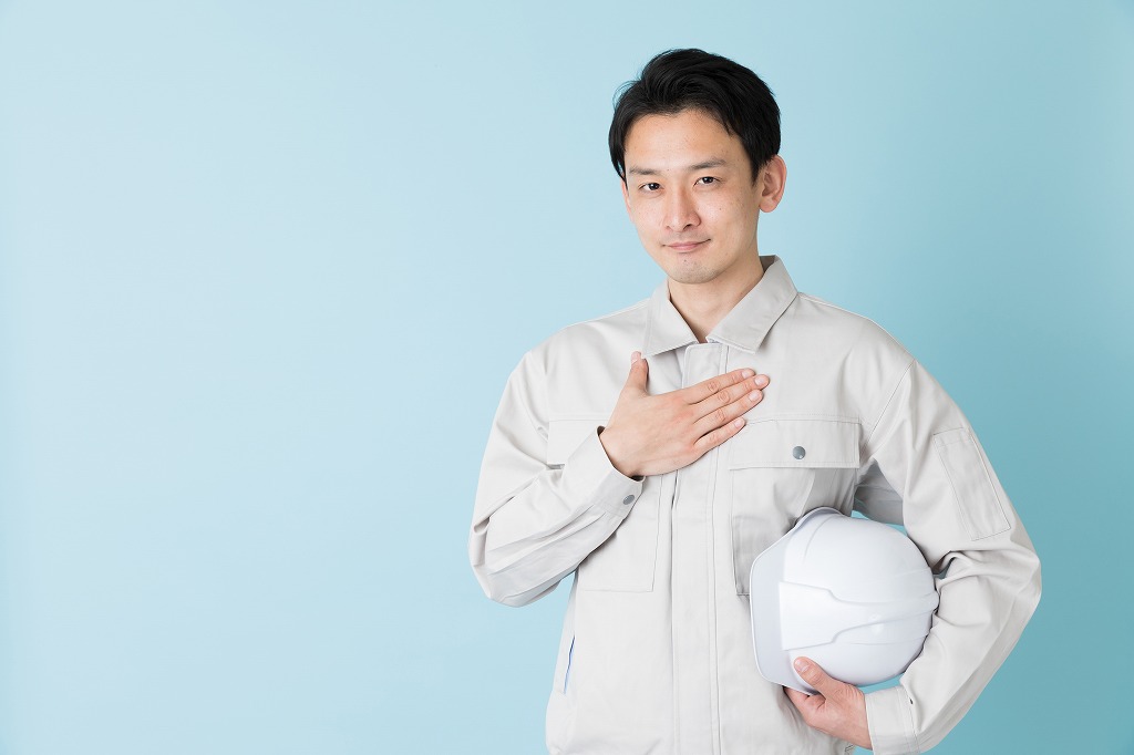 手を胸に当てている作業服の男性